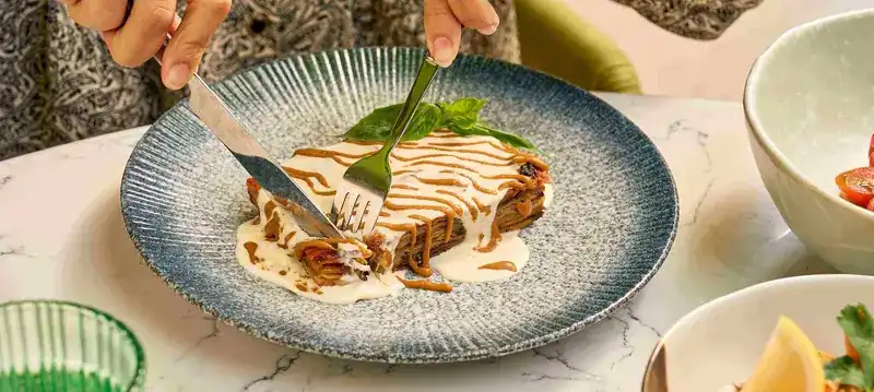 Eggplant parmigiana being cut on a blue plate