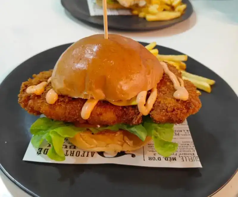 Crispy breaded burger with sauce and lettuce on a dark plate, fries behind