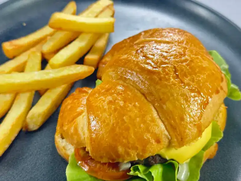 A burger in a croissant bun with cheese and lettuce, fries on the side
