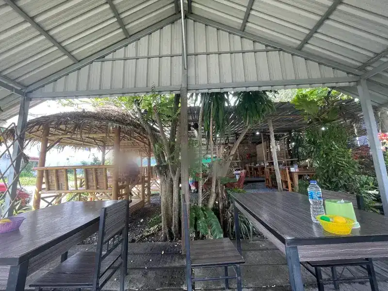 The dining area: tables under a high metal roof, trees growing up through it, and a thatched bamboo sala to the side