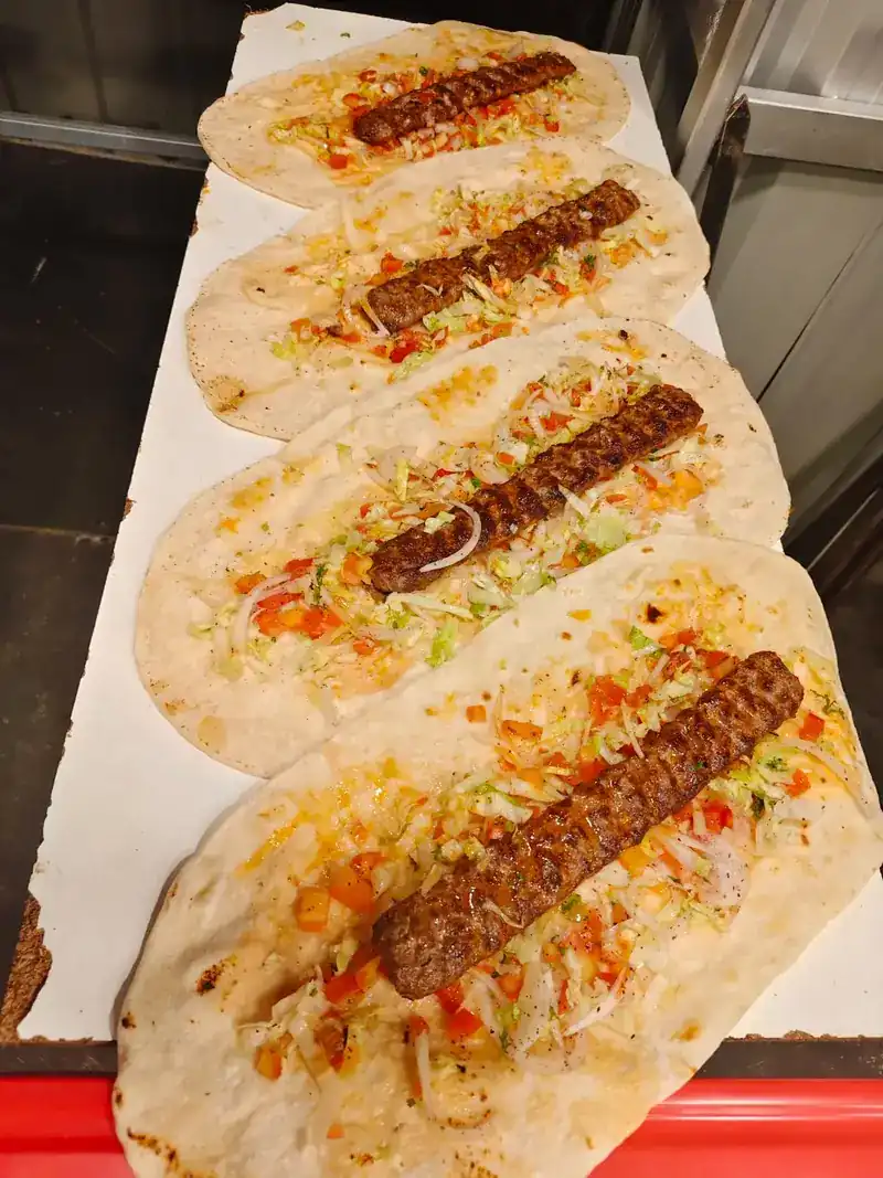 Four Adana kebabs laid on lavash with salad, ready to be wrapped