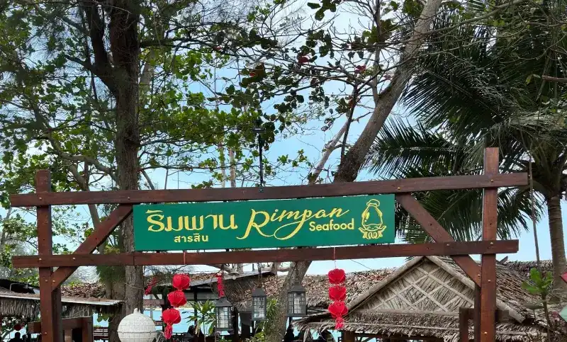 The green Rimpan Seafood sign over the wooden entrance gate, under tall trees