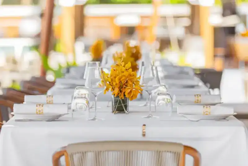 A long white table laid with folded napkins and yellow orchids
