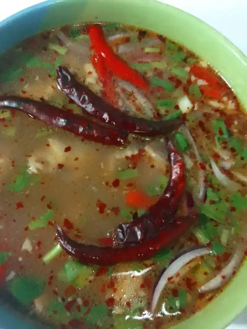 A bowl of hot and sour soup with dried chillies, fresh chilli and herbs