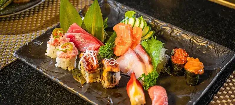 Sushi rolls, sashimi and gunkan on a dark stone plate