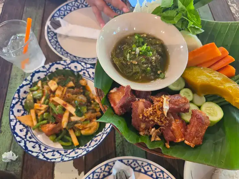 Fried pork with a green chilli dip and fresh vegetables, beside another stir-fried dish