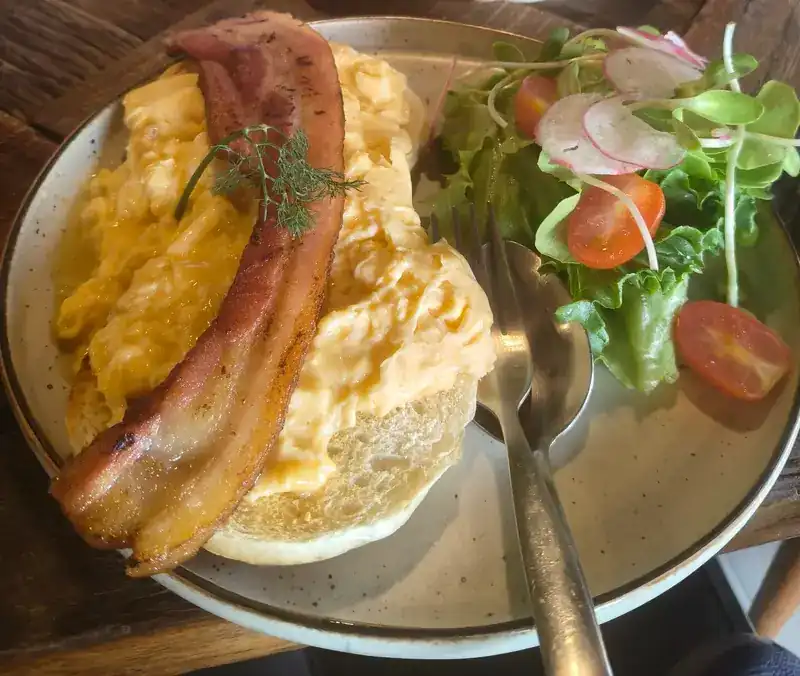 Scrambled eggs and bacon on a bun, with a small salad