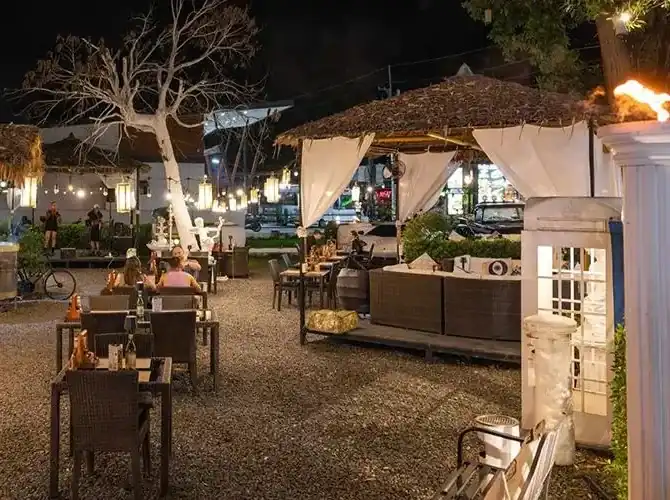 Outdoor tables on gravel under string lights and a thatched cabana at night