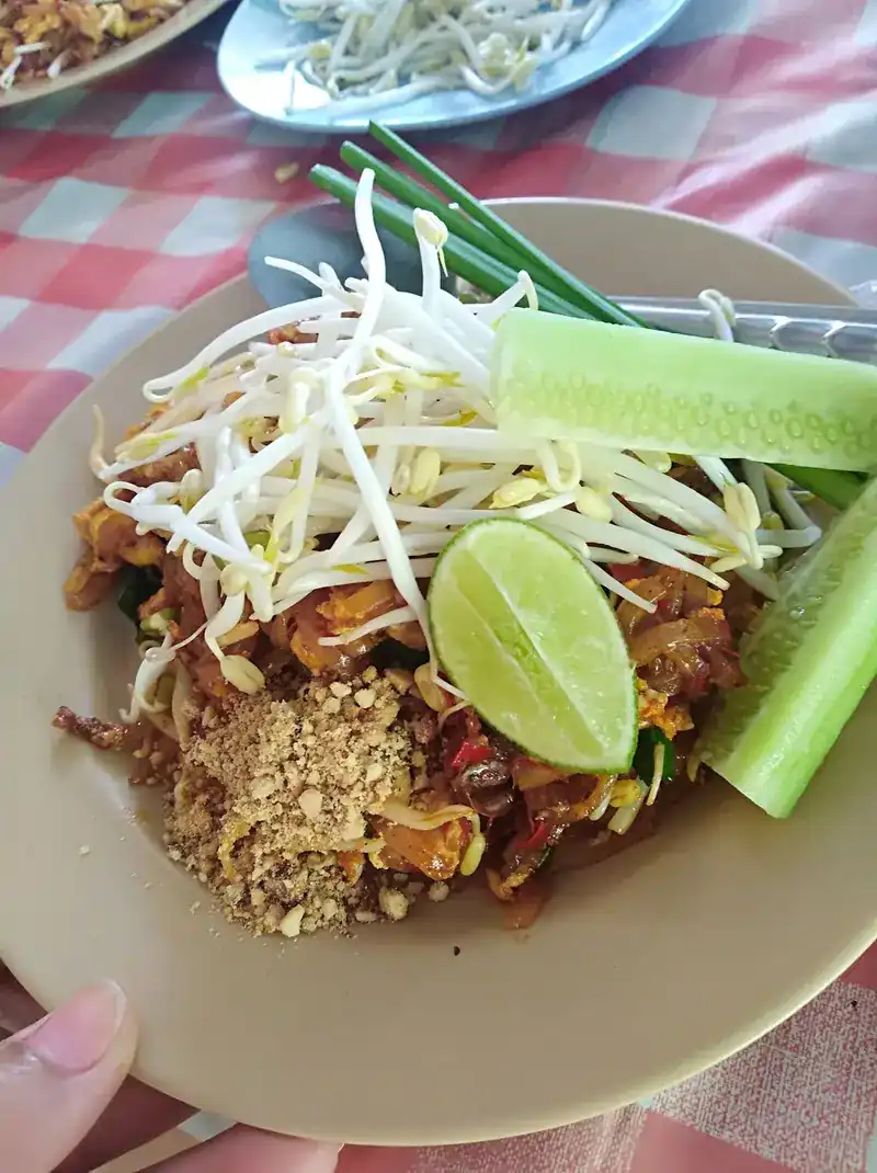 Pad thai topped with crushed peanuts, with lime, cucumber and bean sprouts