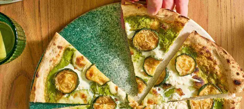 Nerano pizza with zucchini, cut into slices on a green plate