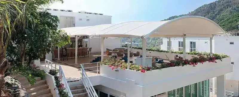 A white rooftop terrace under a curved canopy, with flower boxes and green hills behind