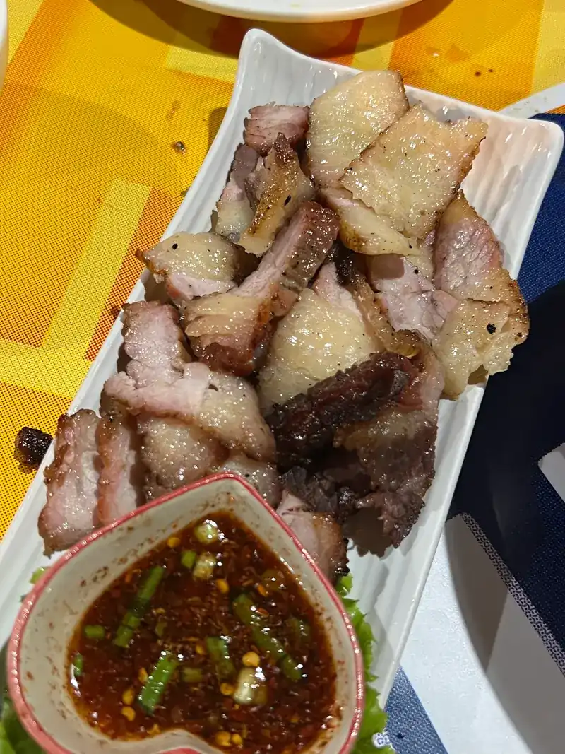 Sliced grilled pork on a long plate with a heart-shaped dish of jaew dipping sauce