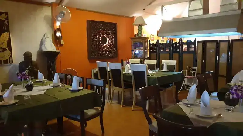The dining room: an orange wall with a carved wooden panel, tables laid with green cloths and folded napkins