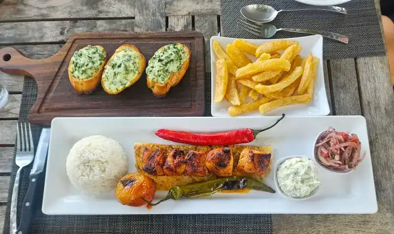 A skewer plate with rice, grilled tomato and pepper and a yoghurt dip, with garlic bread and fries