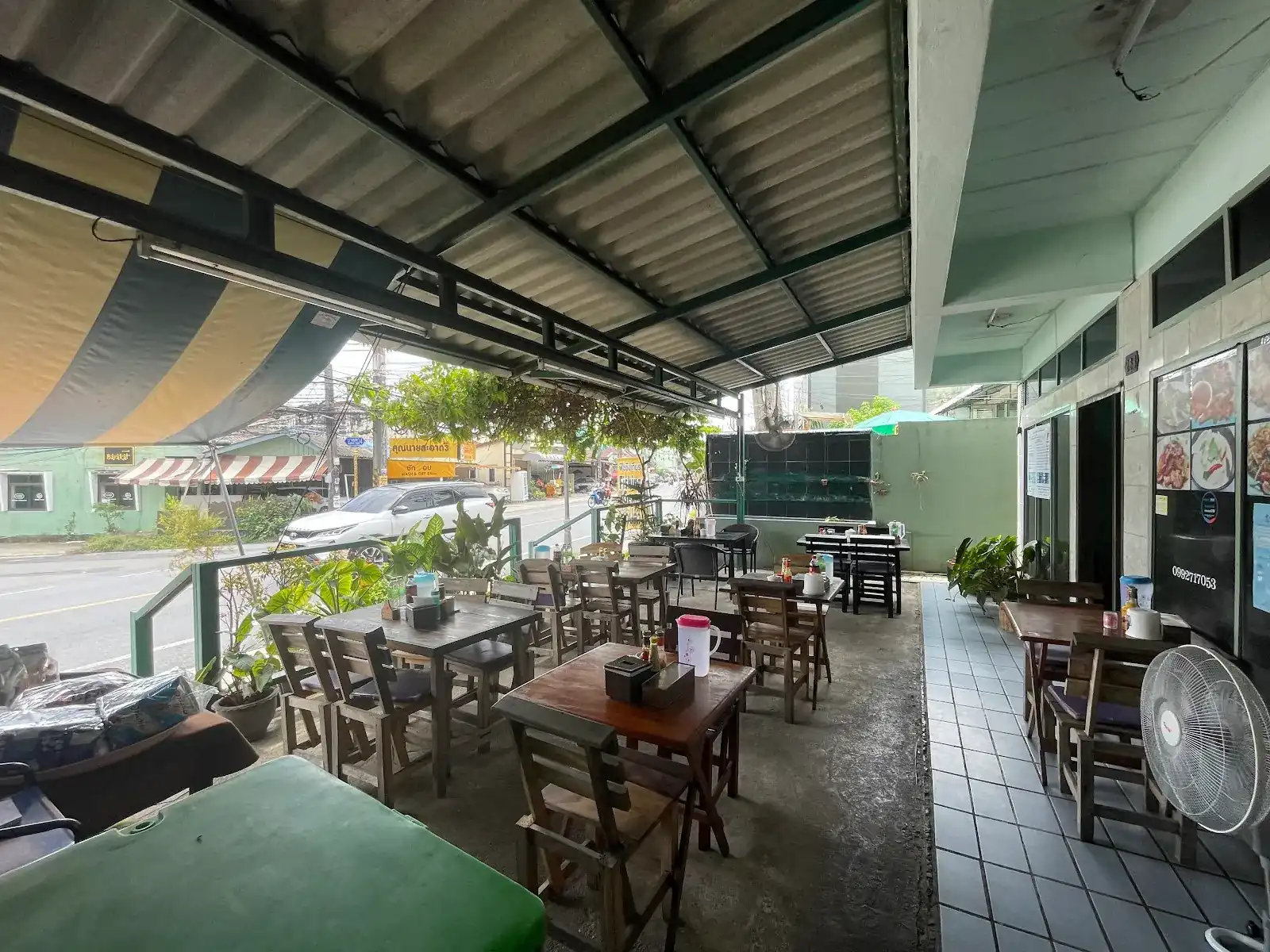 The open terrace of Nui Restaurant: wooden tables under a long roof and a striped awning, beside the road in Choeng Thale