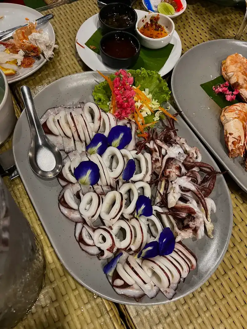 A platter of squid with butterfly-pea flowers, dipping sauces beside it