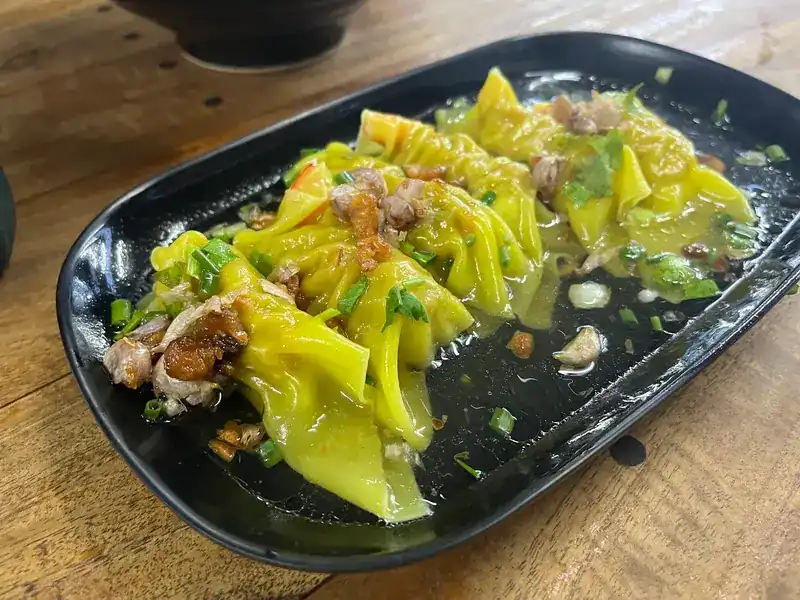 Soft pork dumplings on a black plate with crispy garlic and spring onion / เกี๊ยวหมูบนจานสีดำ โรยกระเทียมเจียวและต้นหอม