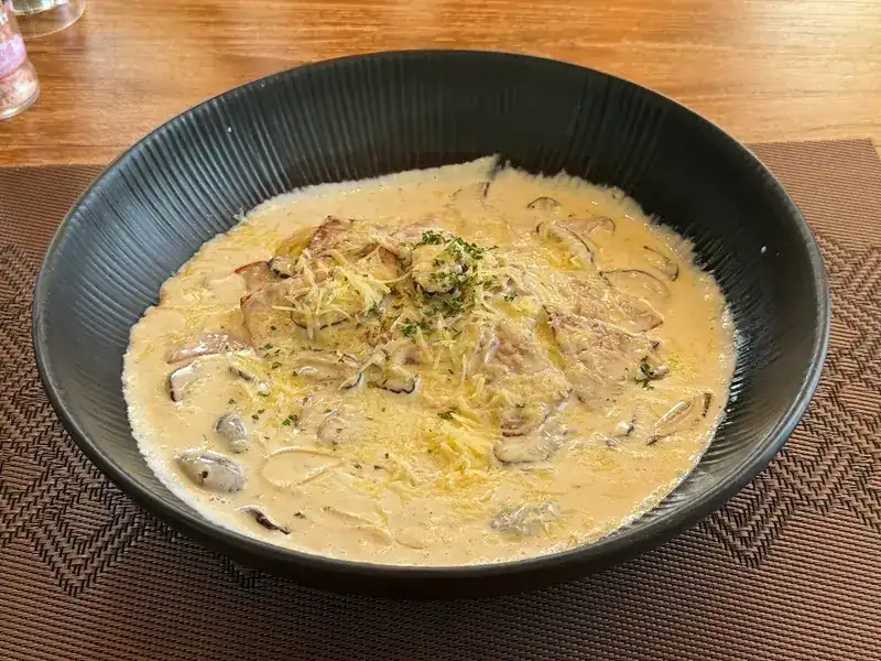 Pasta in a creamy sauce with mushrooms and grated cheese, in a dark bowl