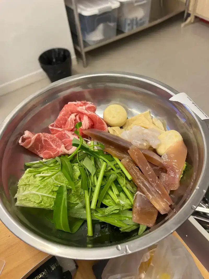 A steel bowl filled at the bar: sliced beef, greens and fish balls