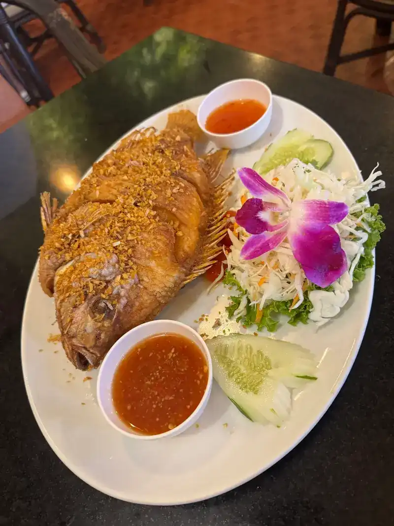 A whole fried fish topped with crisp garlic, with chilli sauce and an orchid