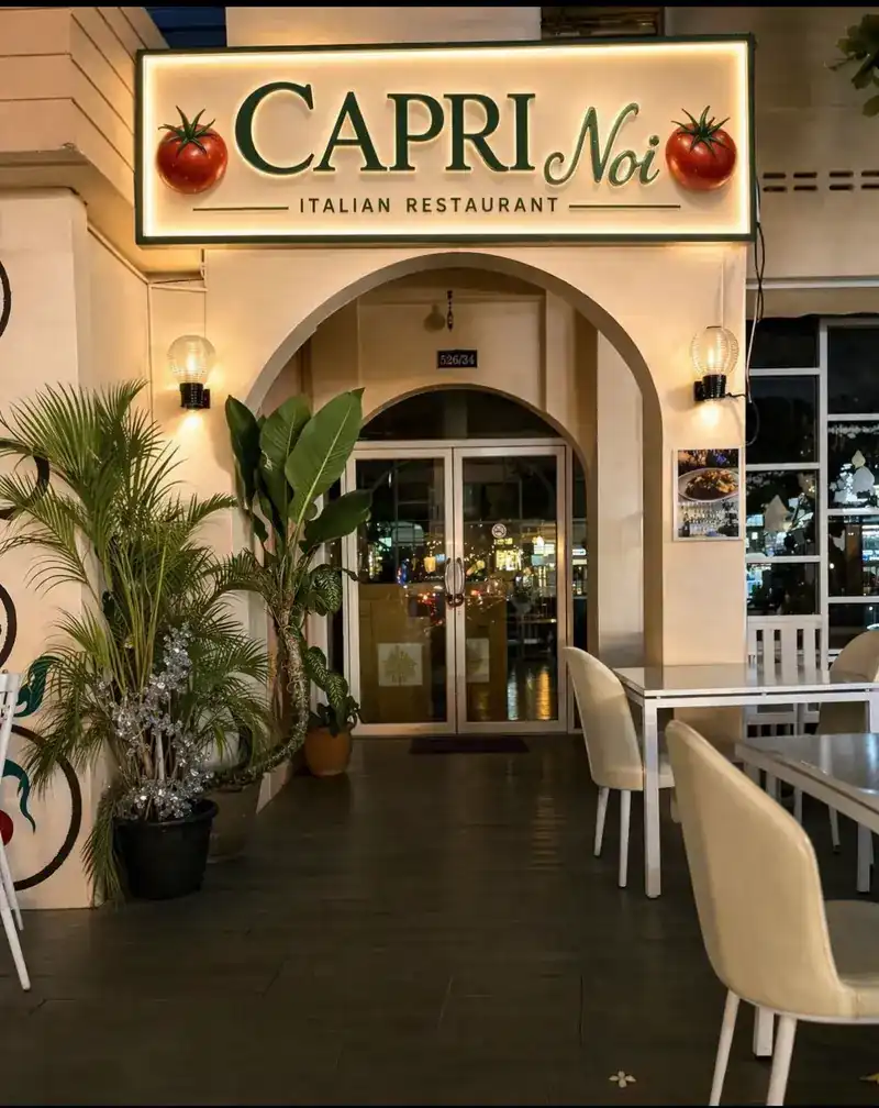 The Capri Noi entrance at night under its lit sign, with tables outside