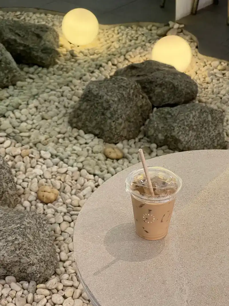 An iced drink on a stone table beside the pebble garden, lit by globe lamps in the evening