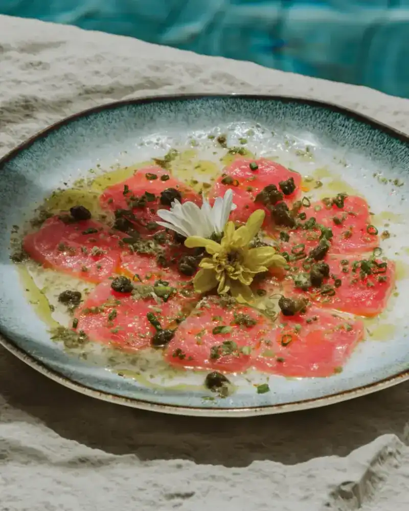 Slices of raw yellowfin tuna with capers and olive oil on a blue-rimmed plate