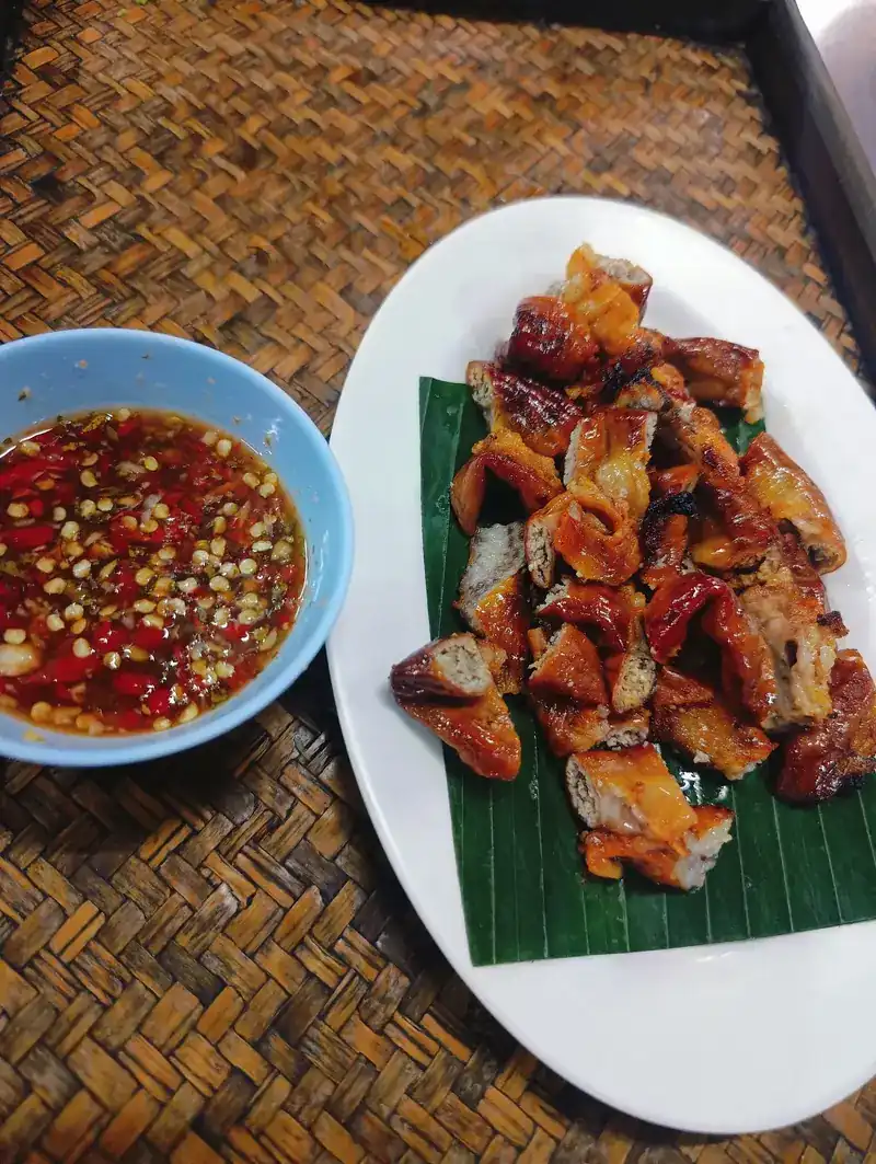 Grilled meat cut into pieces on a banana leaf, with a chilli dipping sauce