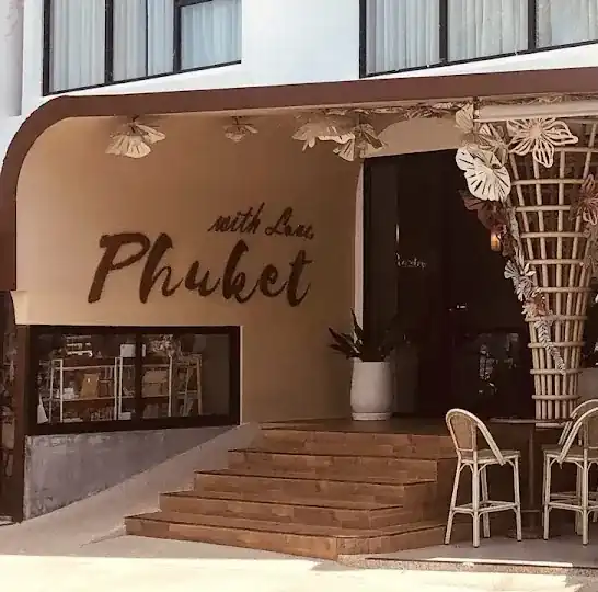The front of Phuket Thai Bistro: a sand-coloured wall with the words with Love, Phuket, wooden steps and a rattan column covered in paper flowers