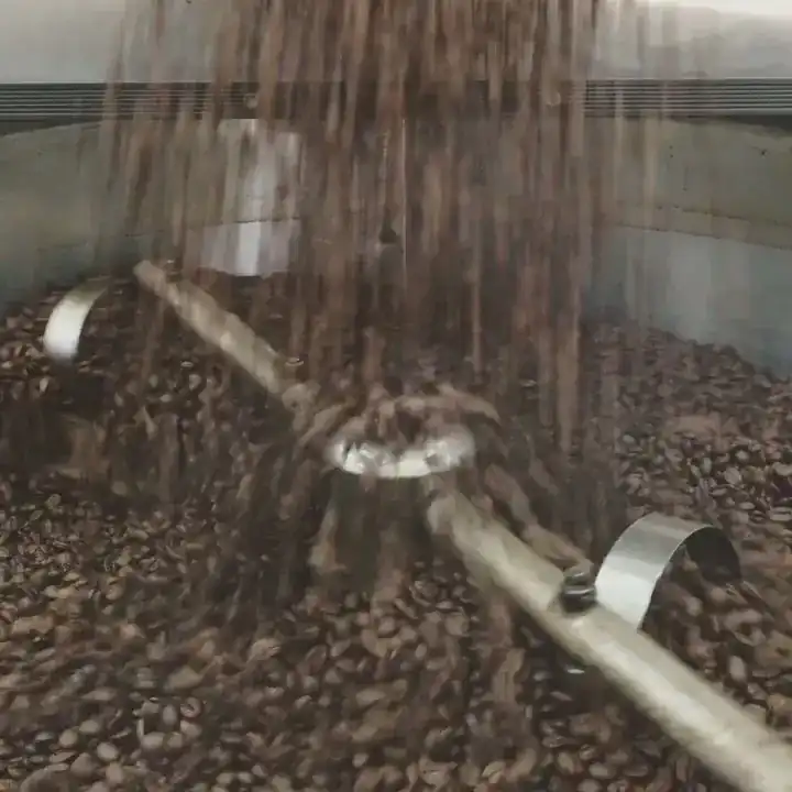 Freshly roasted coffee beans pouring into a roaster’s cooling tray with a turning stirring arm