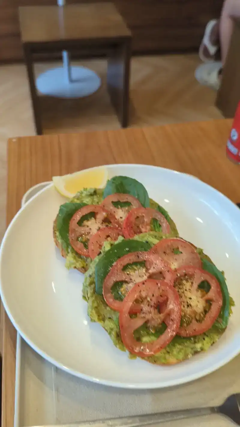Toasted bagel halves topped with smashed avocado, sliced tomato and greens