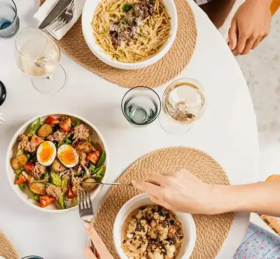 Shared plates on a round white table seen from above, hands reaching in