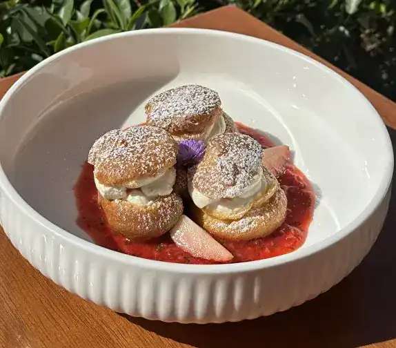 Profiteroles dusted with sugar on strawberry salsa in a white bowl