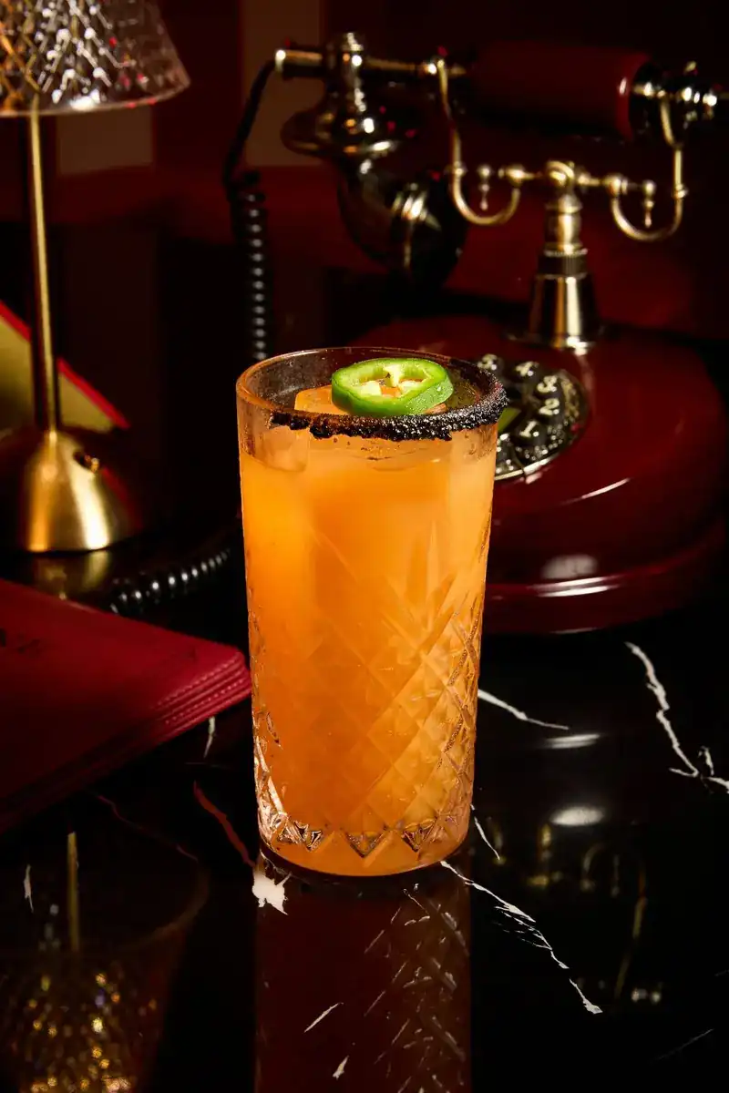 A signature cocktail with a slice of jalapeño beside an old brass telephone