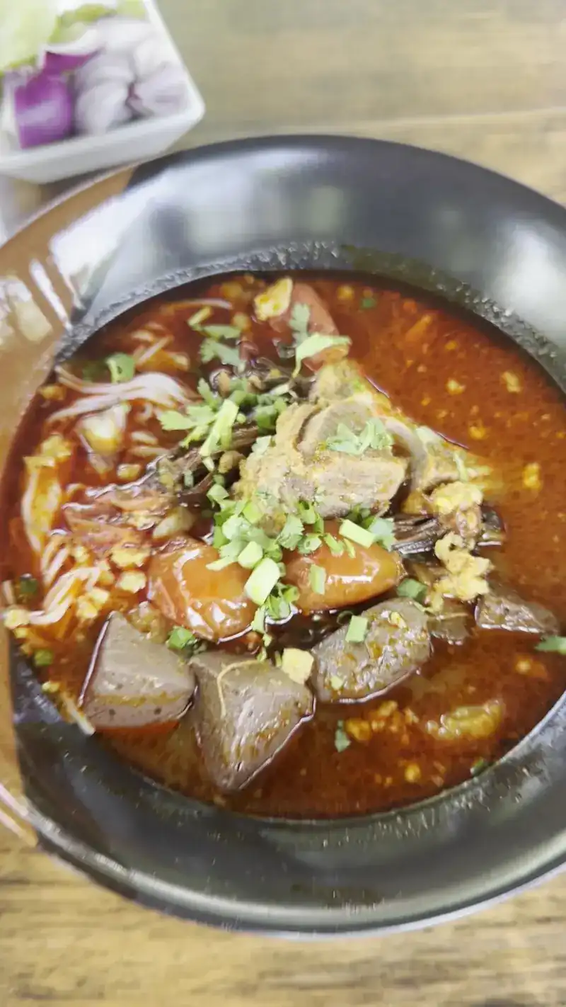 Noodle soup in a dark bowl with blood cubes and spring onion