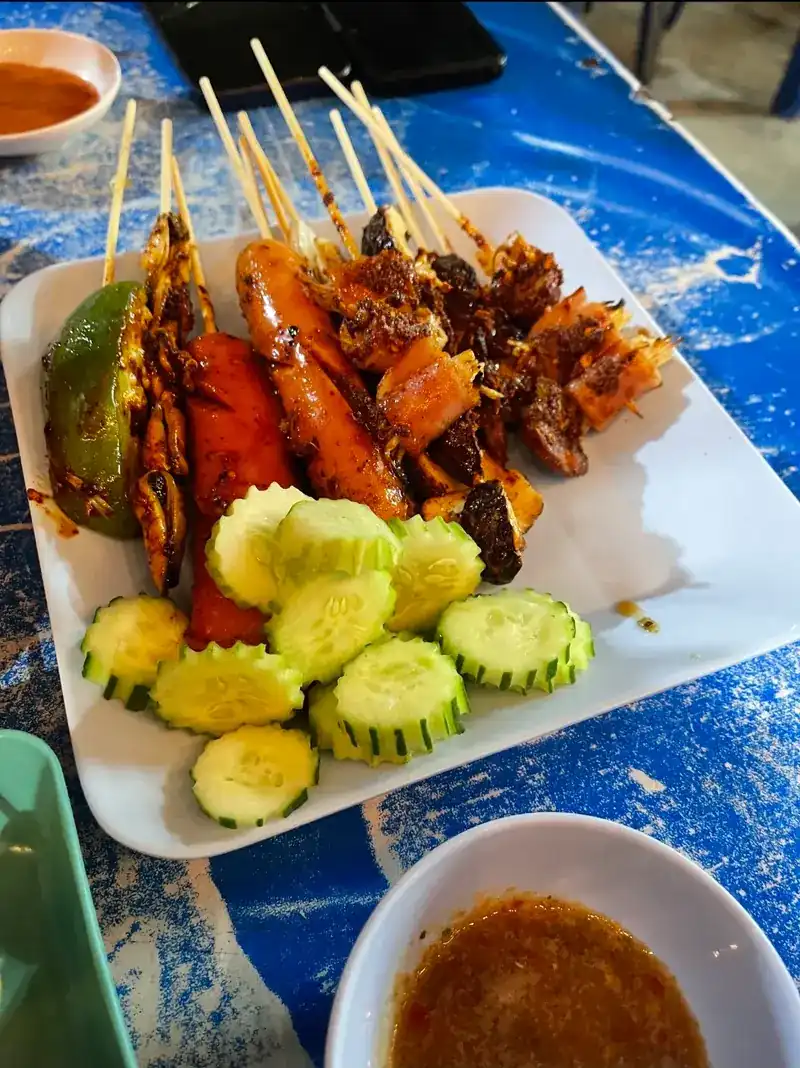 A plate of grilled skewers with cucumber slices and dipping sauce