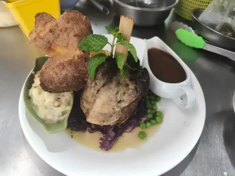 Roast lamb shank with two Yorkshire puddings, mashed potato, red cabbage, peas and gravy