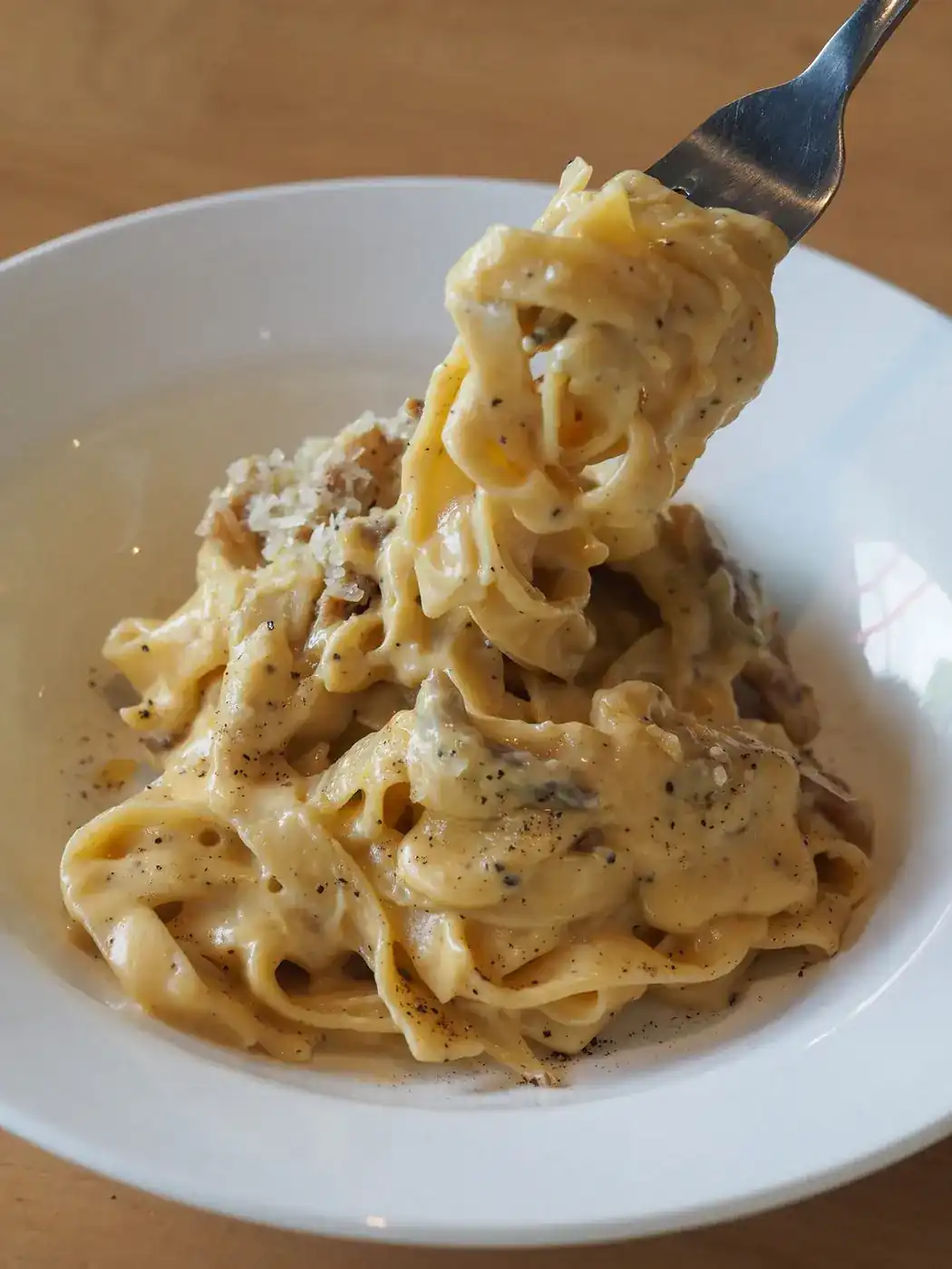 A fork lifting ribbons of fresh pasta in a creamy sauce with black pepper