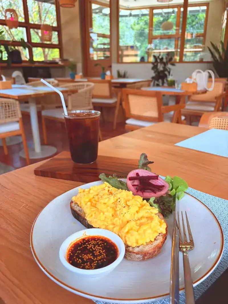 Scrambled egg on toasted bread with a dish of spice oil, and an iced drink