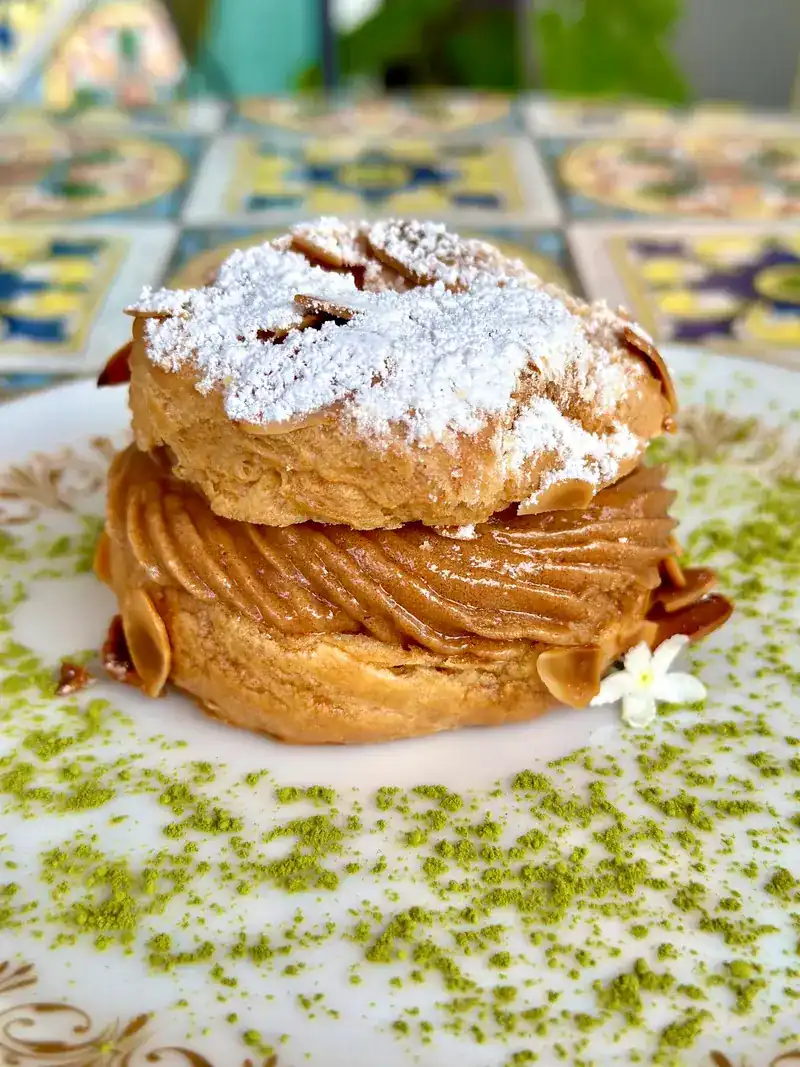 Paris-Brest dusted with sugar and flaked almonds, on a tiled table