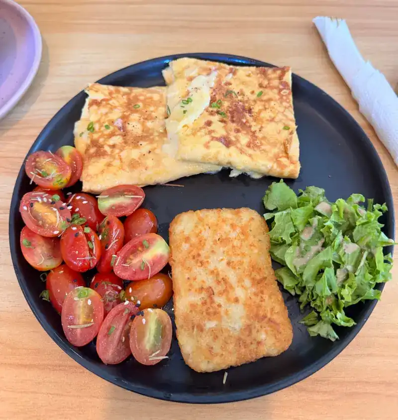 A breakfast plate with an egg dish, cherry tomatoes, a hash brown and salad