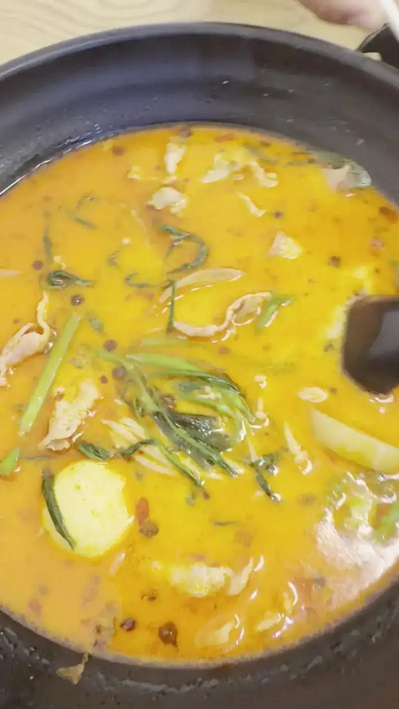 A cooked bowl in a black pot, the broth flecked with chilli