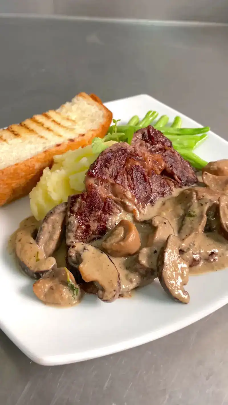 Steak in mushroom sauce with mashed potato, green beans and grilled bread