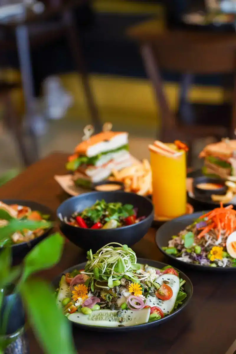 A table of sandwiches with fries and bowls of salad