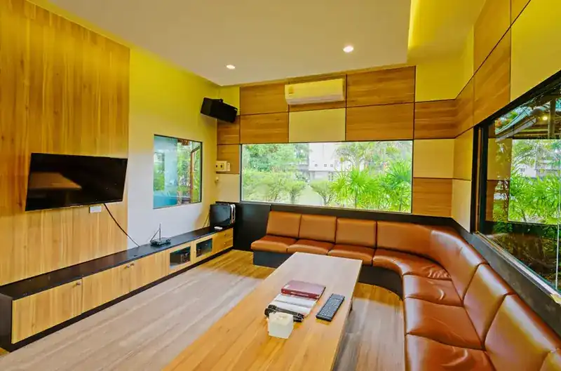 A karaoke room with a long leather sofa, wood panels and a window onto the garden