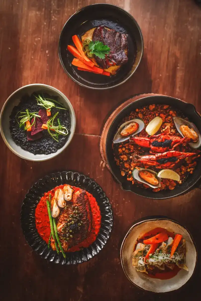 Five plates on a wooden table seen from above, with a pan of rice, prawns and mussels