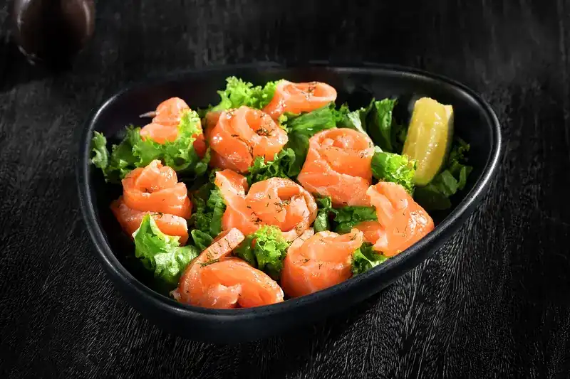 Rolled slices of salmon on green lettuce with lemon in a black bowl