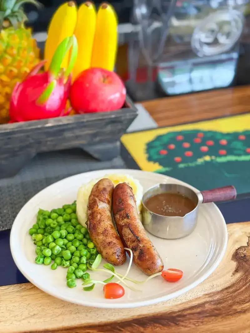 Two grilled sausages with mashed potato, peas and a pot of gravy