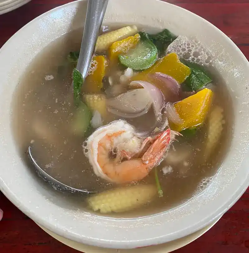A clear soup with a prawn, pumpkin, baby corn and vegetables