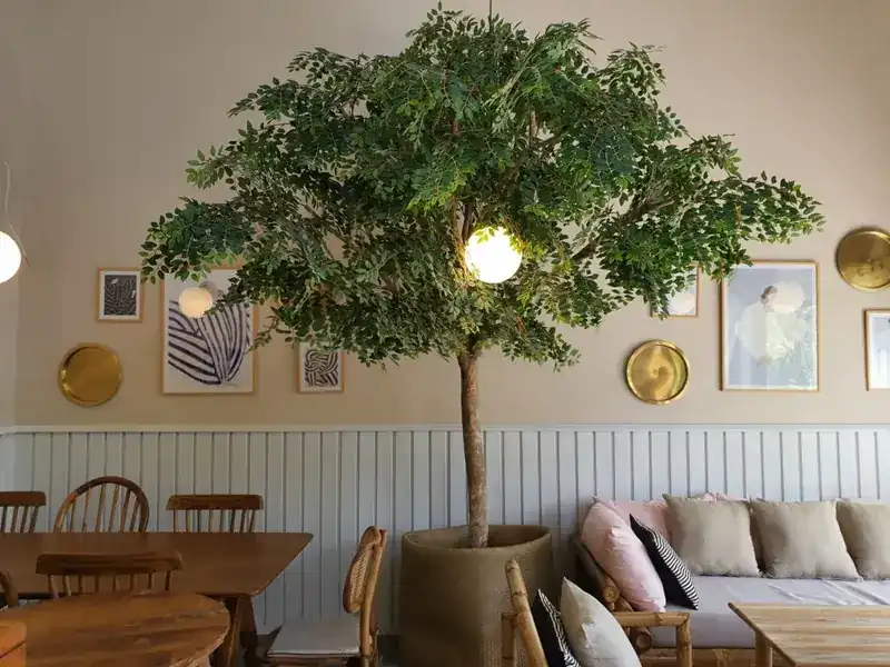 A tree standing indoors among wooden tables, sofas and framed prints